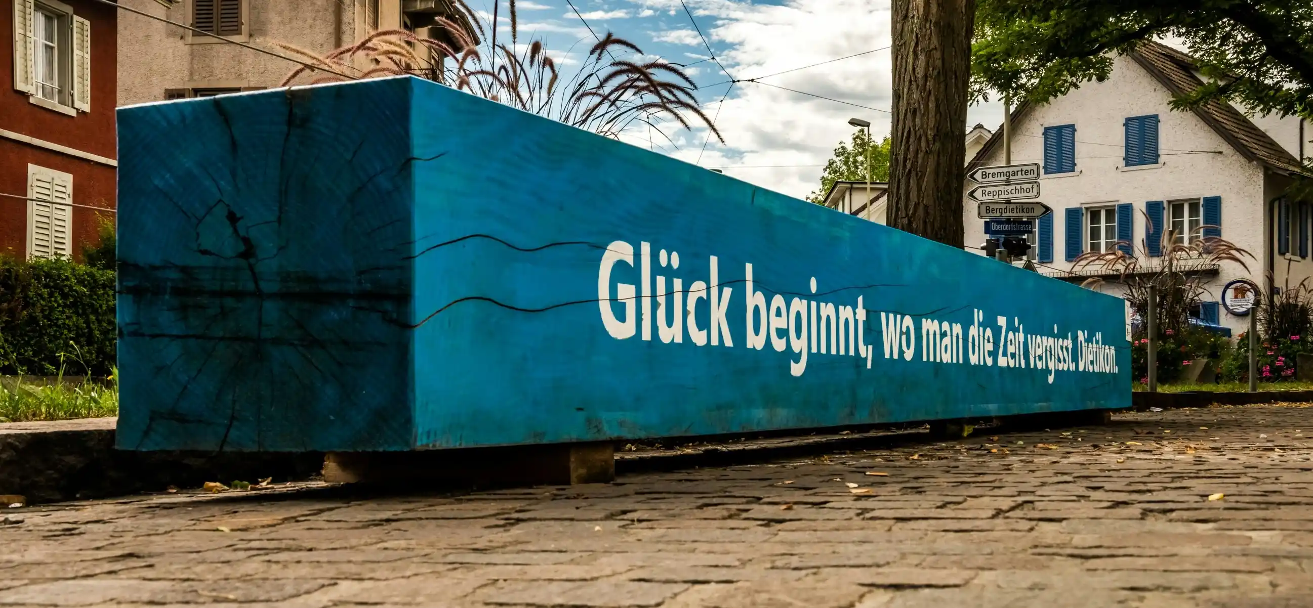 Blauer Holzbalken mit dem Spruch «Glück beginnt, wo man die Zeit vergisst. Dietikon.» an der Oberdorfstrasse - kanalreinigung dietikon